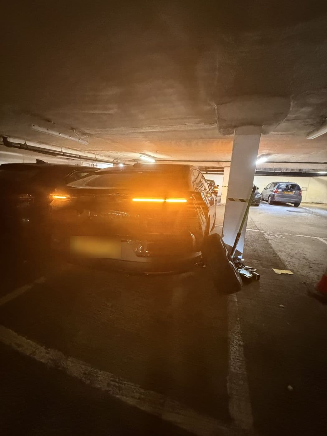 A car in an underground car park at night with a wheel off and the jack beside it
