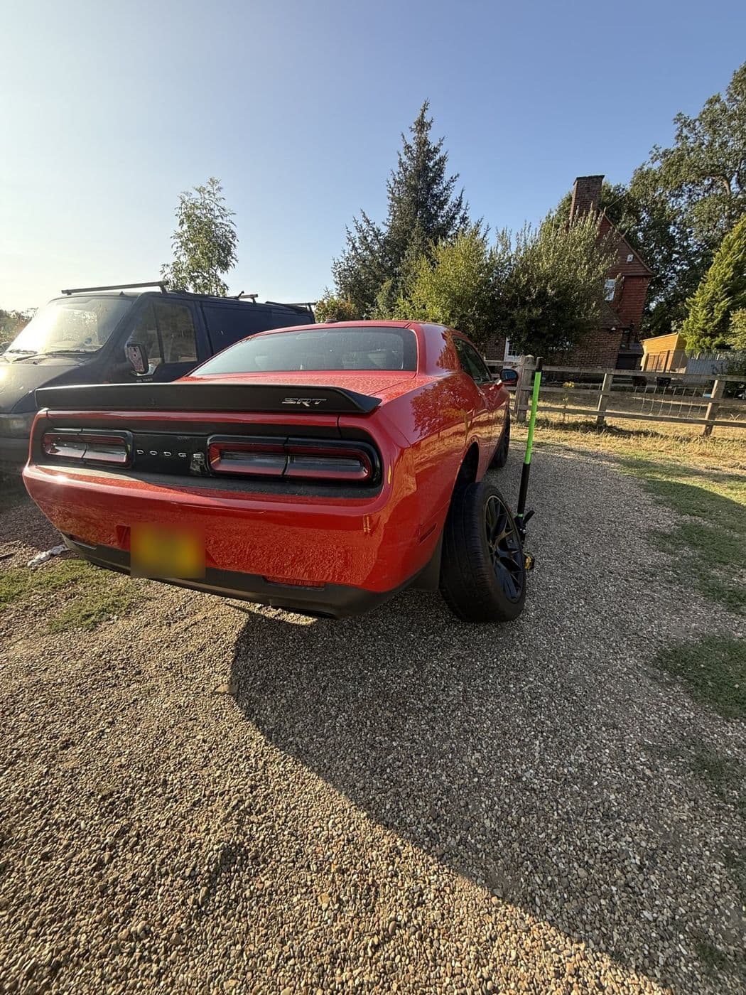 An orange Dodge Challenger on a gravel drive with a trolley jack beside the rear wheel