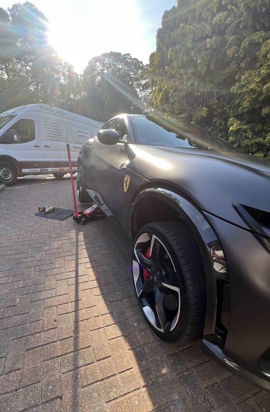 A matte grey Ferrari Purosangue raised on a trolley jack on a block-paved drive